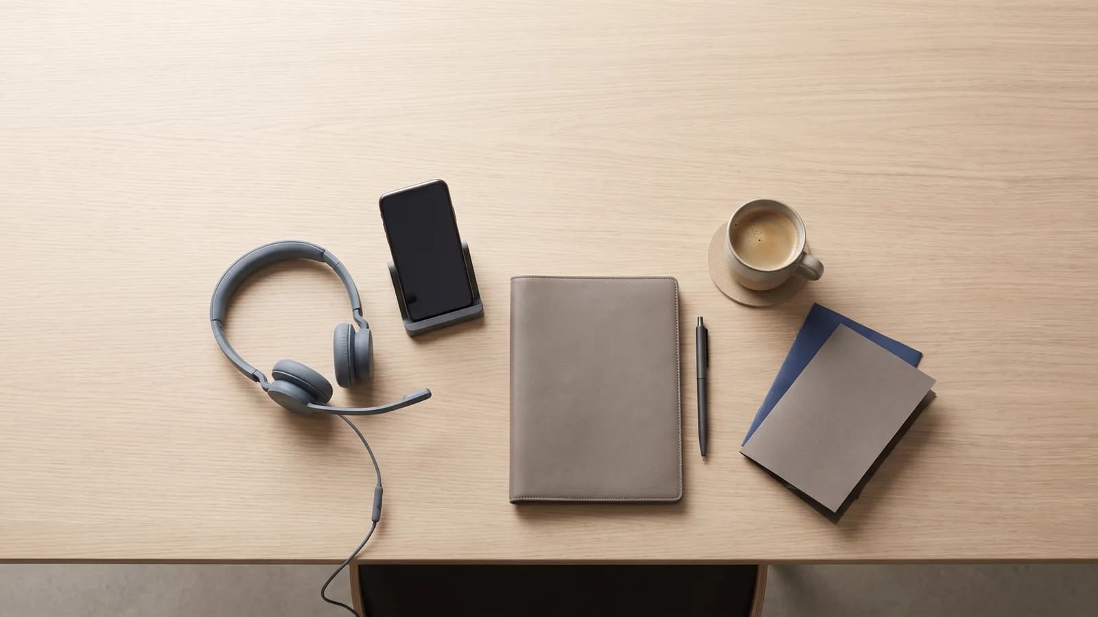 A flat-lay of a Dubai agent's workstation from above: a headset, a phone on a stand with its screen dark, and a notepad in morning light